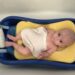 first years sure comfort deluxe baby tub with baby inside of it with a sponge sling and shampo caddy
