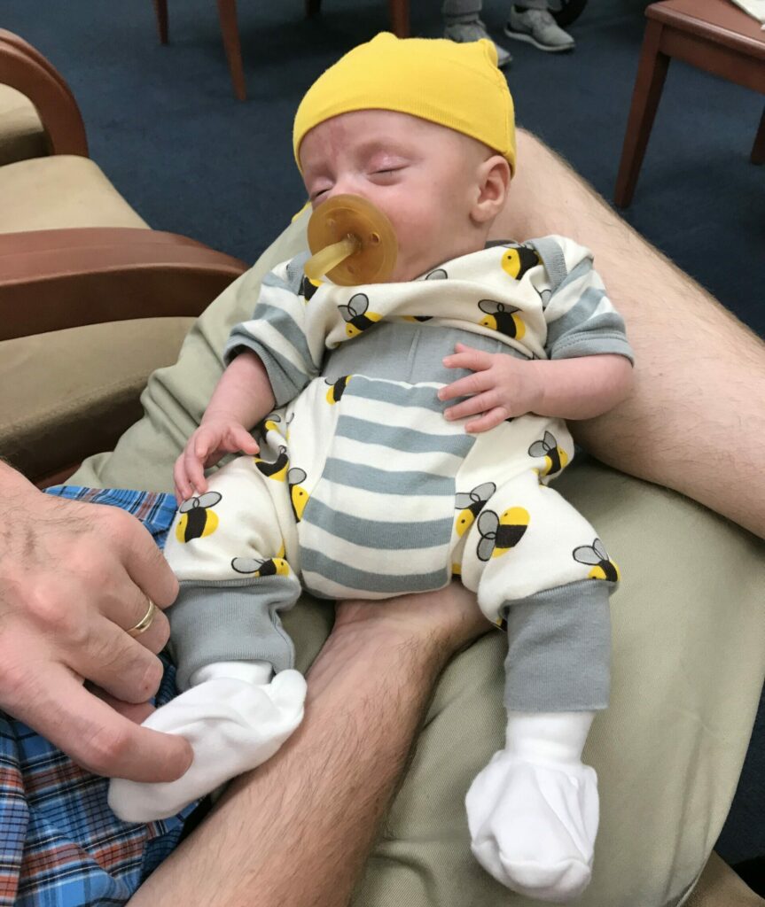 Newborn premature baby boy with a pacifier taking a nap on daddys leg