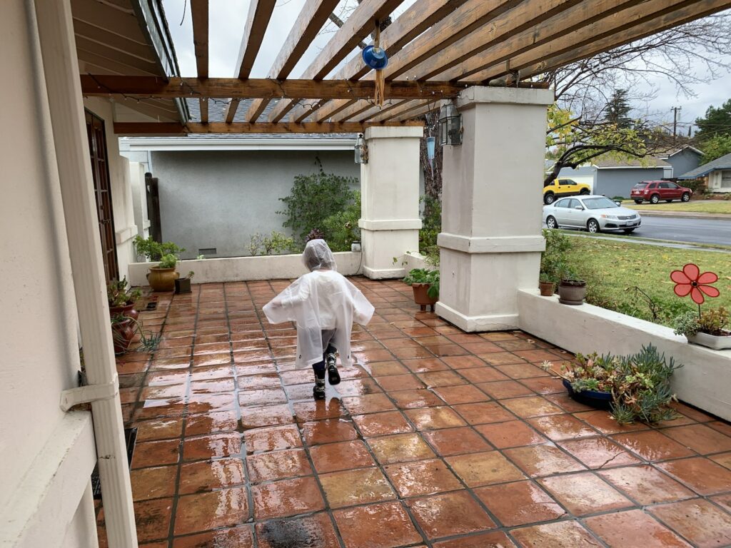Little boy splashing on the porch in rain puddles