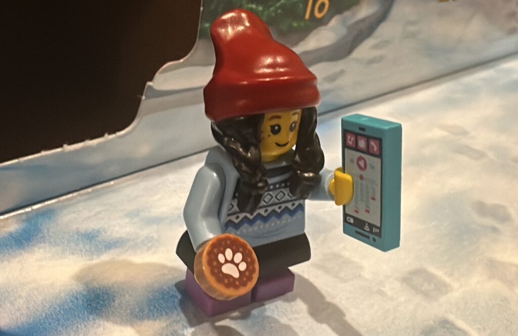 Day 14 Young Girl Minifigure This Tween or Teen is holding a doggie treat or cookie along with her cool smartphone iphone she's adorable in her red beanie and cozy sweater