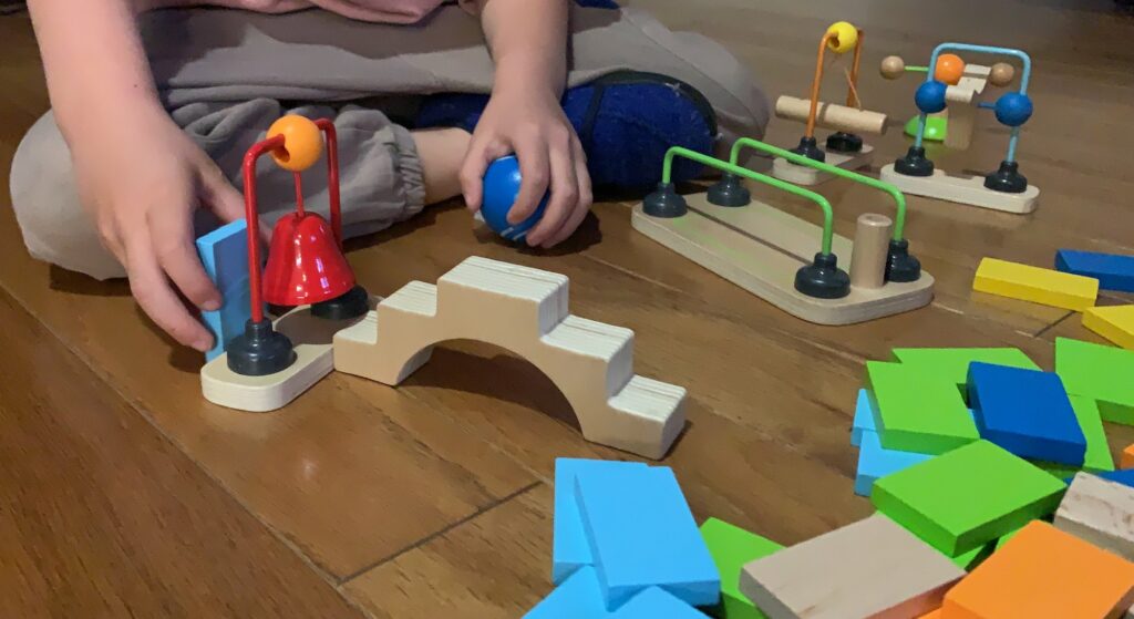 HAPE Wood Domino obstacles include a stair case bridge, red bell, blue ball, swinging log, spinner fidget toy and a spinning arm